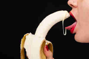 Girl about to swallow a banana with cream on it dripping on her lips
