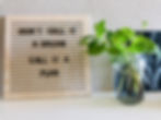 Wooden sign with "Don't call it a dream, call it a plan" text next to a glass jar with mint stems in water, set against a textured wall.