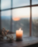 Image of a burning candle on a table in front of a window with baby's breath next to it.