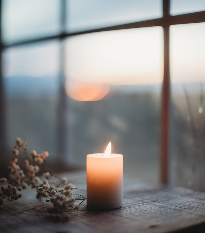 Rustic clay pot with a lit candle, casting a warm glow against a muted yellow background. Calm and serene ambiance.