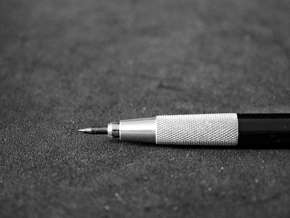 Close-up view of a mechanical graphite pencil with a textured grip, lying on a dark textured surface.