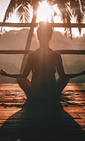 A woman sitting cross-legged doing yoga as the sun rises