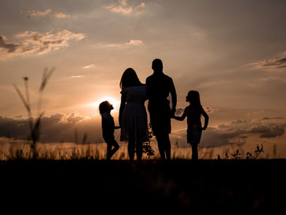 A silhouette of a family holding hands against a sunset, with a father, mother, and two children standing together in a peaceful outdoor setting.