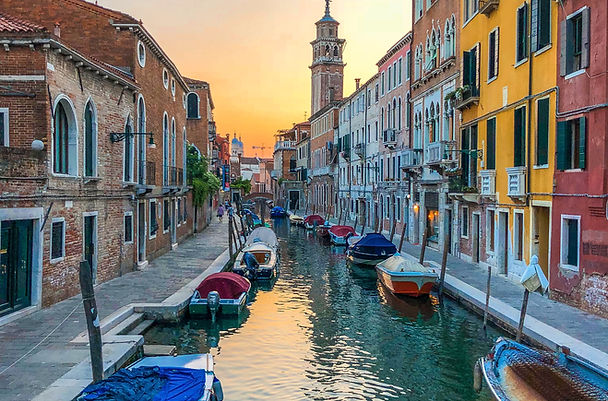 "The sun rises, painting the buildings along a quaint Venetian canal with a warm and captivating glow."