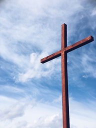 Wooden cross against a vibrant blue sky with wispy clouds. Strong vertical composition, evokes a sense of peace and spirituality.