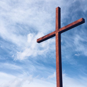 Cruz de madera contra un cielo azul con nubes esponjosas. La escena transmite serenidad y espiritualidad. Sin texto visible.