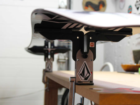 Snowboard base facing up on a workbench with edge tuning tools, demonstrating end-of-season snowboard maintenance and how to store a snowboard for the off season
