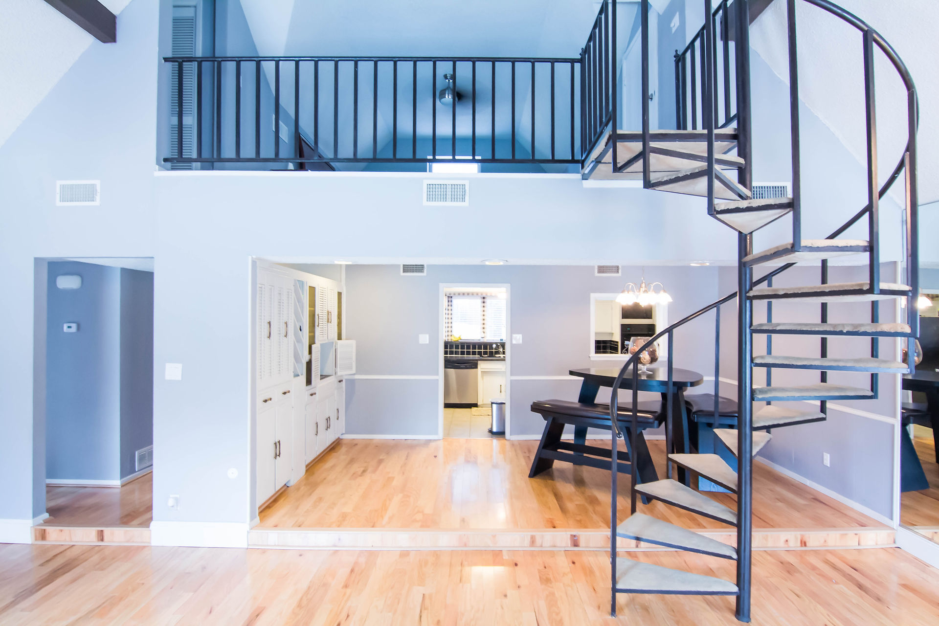 Spiral staircase in a bright, blue-toned house with parquet flooring, overlooking the kitchen and dining room.