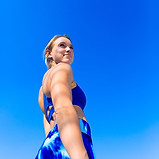 Confident athletic woman in blue activewear looking upward against a clear blue sky, symbolizing strength and motivation