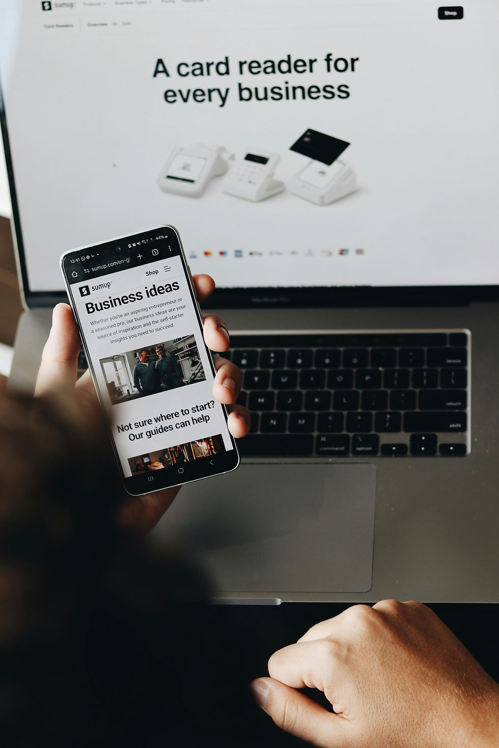 Exploring business ideas on a smartphone while a laptop screen highlights versatile card readers for entrepreneurs.
