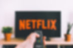 A hand holding a remote control aimed at a television with "Netflix" on the screen