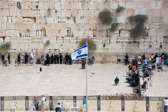 Menschen beten an der Klagemauer, viele tragen Schwarz. Eine israelische Flagge weht. Stimmung ruhig und andächtig.
