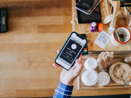 Hand holding a smartphone with a payment app, wooden table, colorful cups, QR code, and phone on the side. Casual, modern setting.