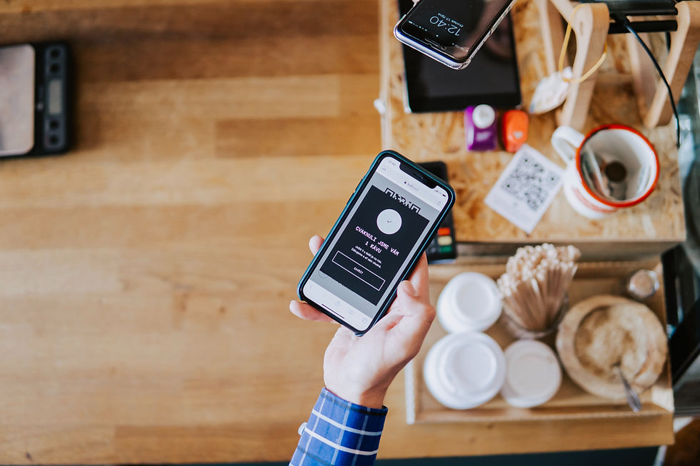 Hand holding a smartphone with a payment app, wooden table, colorful cups, QR code, and phone on the side. Casual, modern setting.