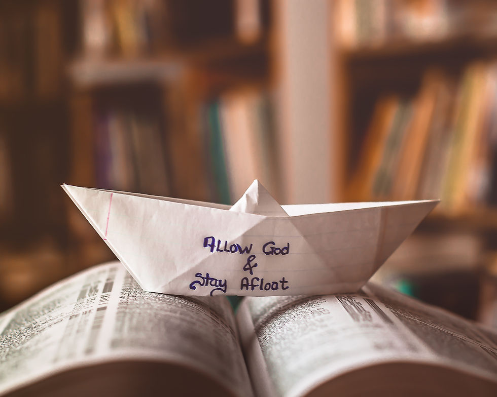 Paper boat with handwritten note on front reading, "Allow God & stay afloat," sitting atop an open book