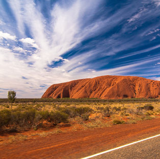 A breathtaking view of Uluru under a dramatic sky, highlighting the iconic red sandstone against Australia's arid Outback.