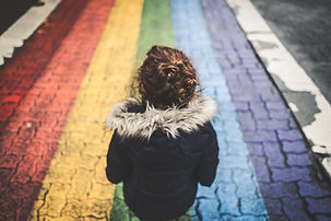 A young child has their back to the camera standing on a road that is painted as a rainbow - red, orange, yellow, blue, violet