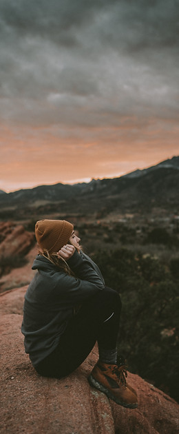 a woman sits on a hill with her hands on her chin thinking about life