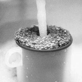 An overfull cup of water with more water still pouring into it.