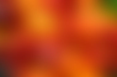 A vibrant pile of red, orange, and yellow bell peppers fills the frame. The smooth, glossy surfaces and rich colors convey freshness and abundance.