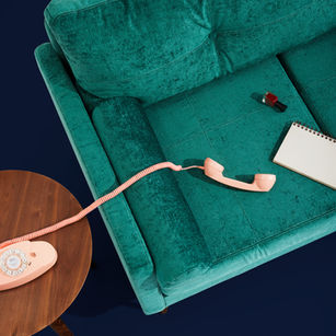 A teal sofa with a peach rotary phone, notepad, and nail polish. The phone's cord is stretched across the sofa on a wooden table.