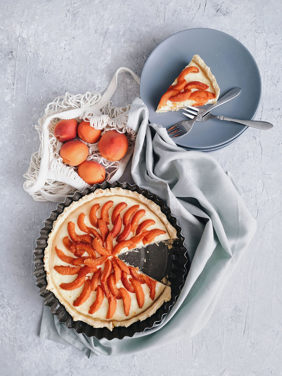 Cheesecake fondant à l’abricot servi dans un moule noir avec parts découpées, abricots frais et assiettes grises sur une table claire.