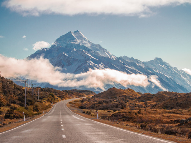 Strada panoramica verso il Monte Cook in Nuova Zelanda, con montagne innevate e nuvole basse.