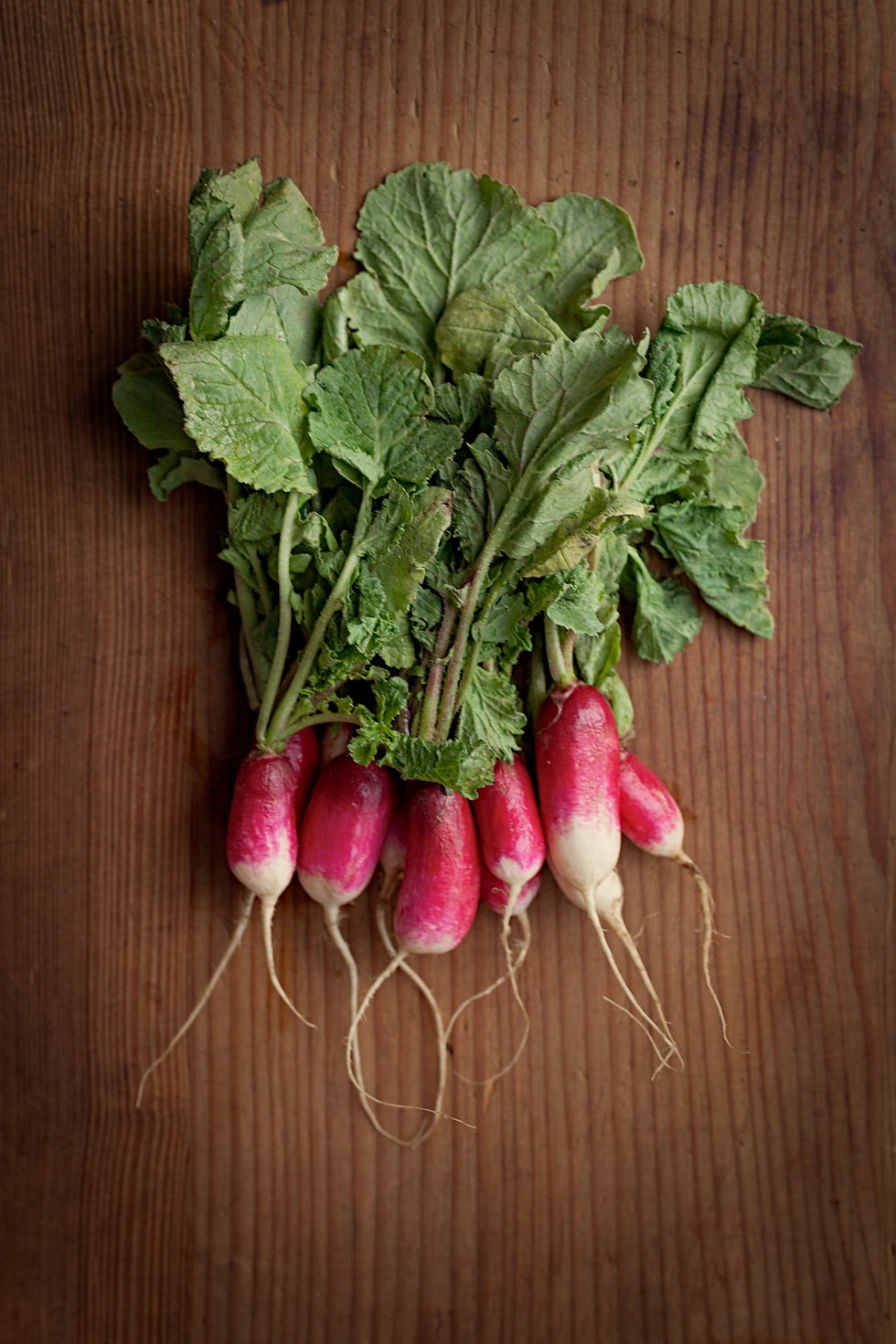 Fresh pink and white radishes with green leaves lie on a wooden surface, showcasing their vibrant colors and textured leaves.