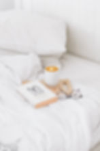 A coffee, glasses and a book lie on a bed which is made up with clean, white bedding