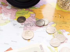 Coins scattered on a colorful map of India and China, with country labels and a magnifying glass edge visible.