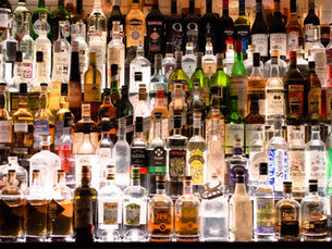 A variety of liquor bottles are displayed on backlit shelves, showcasing diverse labels and vibrant colours in a bar setting.