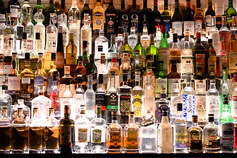Shelves filled with colorful liquor bottles in a dimly lit bar. Various labels displayed on vodka, rum, and whiskey bottles.