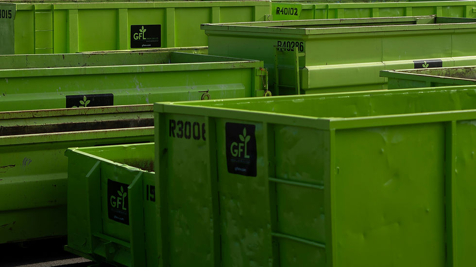 Rows of bright green dumpsters with black logos and numbers, lined up outdoors in a cluttered industrial lot.