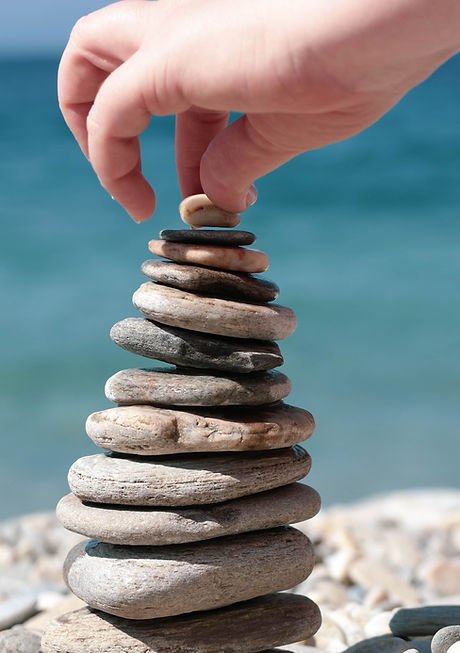 Runde Steinskulptur im Gleichgewicht auf glattem Untergrund am Meer. Hand, die einen Stein oben auflegt und versucht die Steine in Balance zu halten