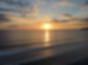 This image shows a golden sunset over the ocean with the sun reflecting on the ocean with a montains on the side.