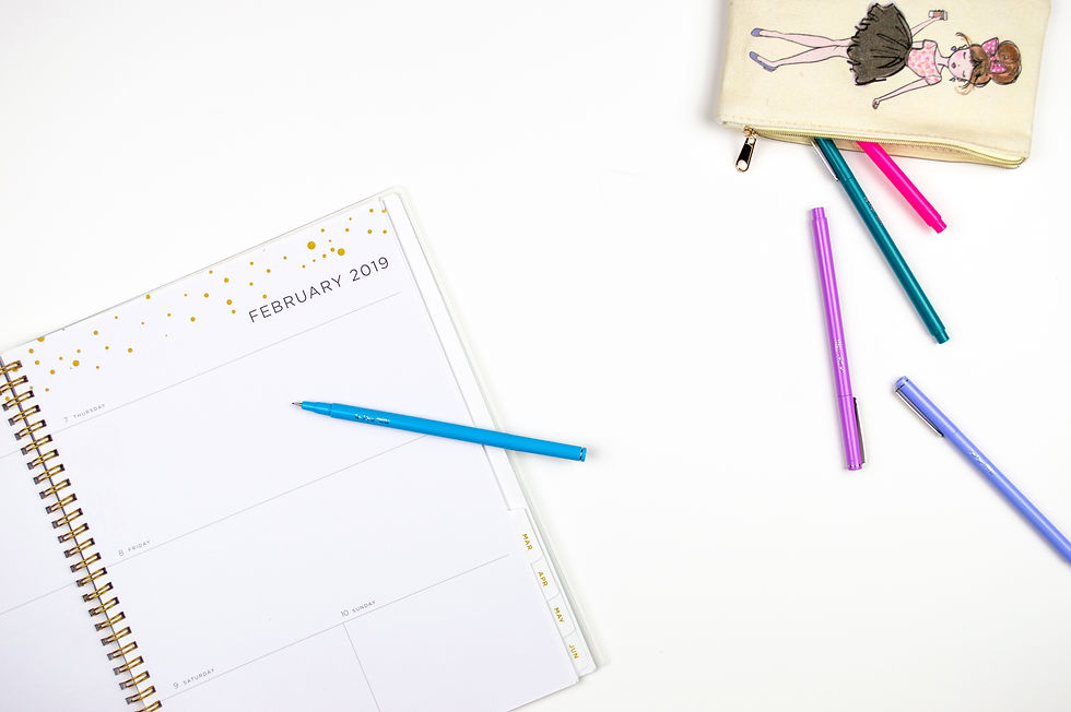 a gold and white planner on a plain background with colorful writing implements nearby
