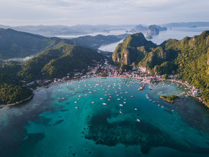 Aerial view of El Nido's turquoise bay surrounded by lush green mountains and boats docked near the shore in Palawan, Philippines.