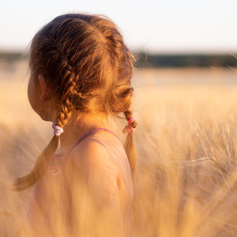 Mała dziewczynka z warkoczami stojąca w złotym polu zboża – symbol wewnętrznego dziecka, niewinności i utraconego poczucia bezpieczeństwa