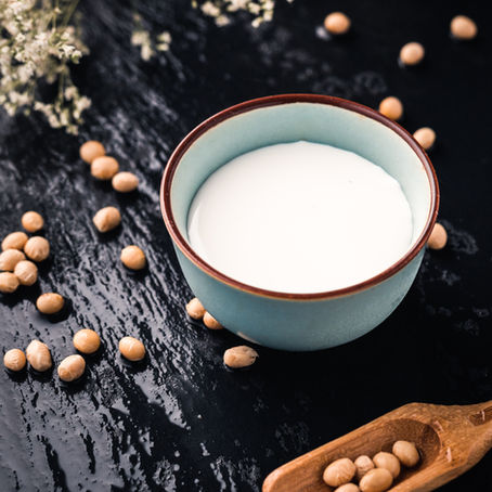 Bowl of milk with scattered soybeans and flowers on a dark textured surface, a calm rustic still life.