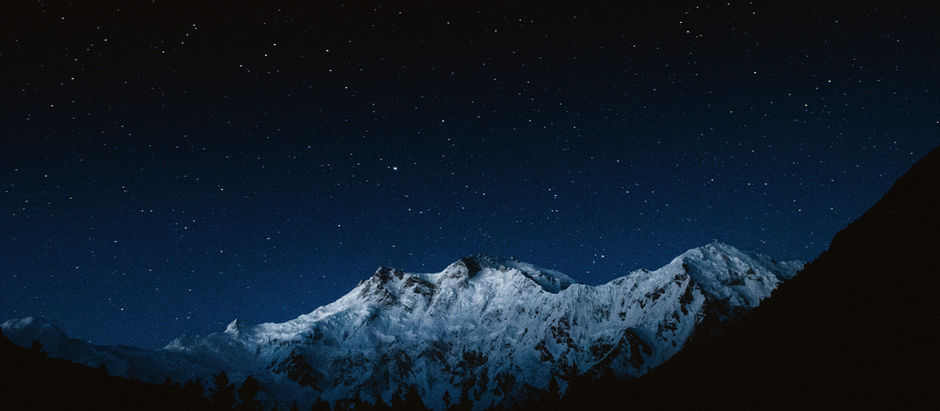 Snowy mountain peaks under a star-filled night sky, glowing blue in a serene, dark landscape.