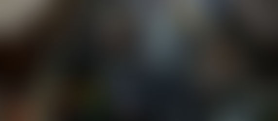 Bustling indoor market scene with people dining and shopping. Stained glass windows, colorful flags, and food stalls create a vibrant atmosphere.