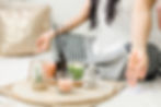 Person meditating with folded legs, hand in mudra gesture. Tray holds candles, stones, and plants. Peaceful atmosphere with soft tones.