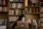 A teen girl writing on a laptop with bookshelves behind her