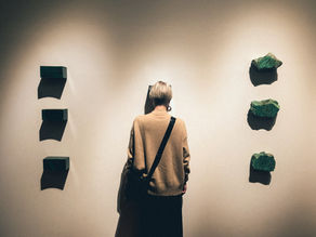 A woman presses her forehead to a museum wall looking desolate. 