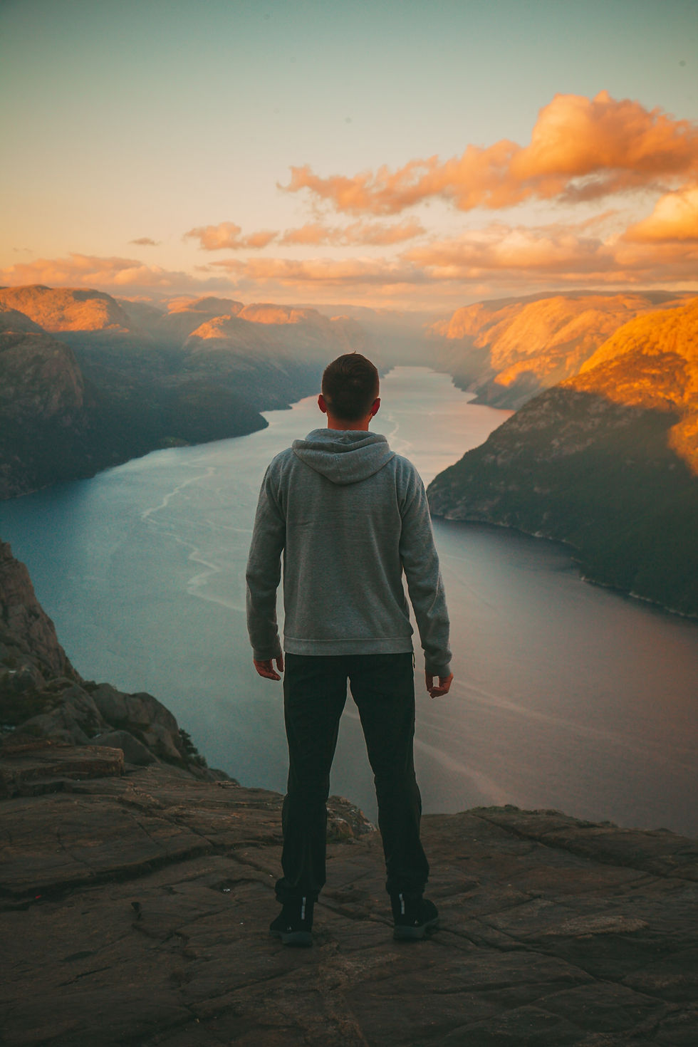 the backside of a man looking outward over a cliff with a river running in front of him