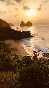 The beach and ocean glow orange under a sunset at Fernando de Noronha
