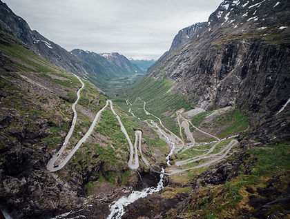 Explore Norway’s western fjords on an eight-day small-group journey combining coastal scenery, historic towns, local food and comfortable accommodation. Starting in Bergen and finishing in Trondheim, the itinerary follows the coast through fishing villages, Art Nouveau architecture, mountain passes and some of Norway’s most celebrated landscapes.
In Kalvåg, stay for two nights at Knutholmen, a collection of traditional sea houses overlooking the harbour. A local family introduces you to the village’s fishing heritage, including traditional rope-making, restored wooden boats and local herring. A boat excursion to Værøya Island offers a closer look at coastal life, with opportunities to try fishing and set crab pots before enjoying a seafood lunch.
Further south, discover Ålesund’s distinctive Art Nouveau buildings before cruising through UNESCO-listed Geirangerfjord, known for its steep mountain walls and waterfalls. The journey continues over the Trollstigen mountain pass, with stops at Dalsnibba and Flydalsjuvet for views across the fjord and surrounding peaks.
In Åndalsnes, ride the Golden Train through the Romsdalen Valley, passing waterfalls, rivers and the towering Troll Wall. A gondola ride and lunch overlooking Romsdalsfjord add another perspective on the landscape. The final days in Trondheim explore regional food traditions, a local farm, and the ruins of King Sverre’s medieval castle. This trip suits travellers who appreciate scenery, history and regional cuisine without a demanding physical itinerary.