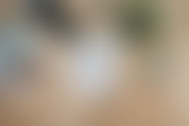 A imagem mostra uma mesa de madeira clara com itens relacionados à criação e planejamento de marketing. No centro, há uma folha de papel com a frase "Marketing Strategy" escrita, sugerindo o tema principal. Ao redor, livros sobre marketing e precificação, marcadores coloridos, uma fita adesiva, um grampeador e uma planta compõem o cenário. O visual transmite uma vibe criativa e dinâmica, indicando o trabalho de brainstorming ou desenvolvimento estratégico em marketing