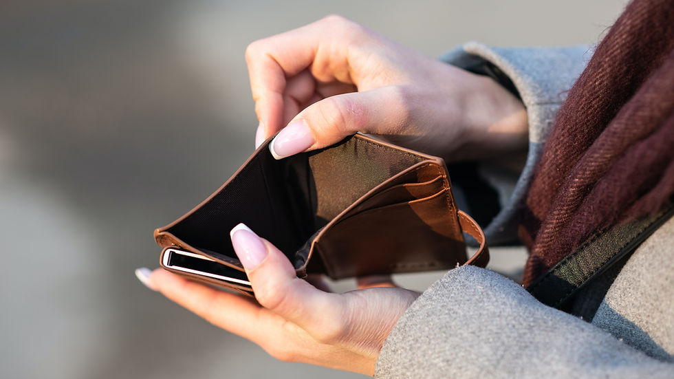 Close-up of hands opening an empty brown wallet, suggesting worry, against a blurred gray background.