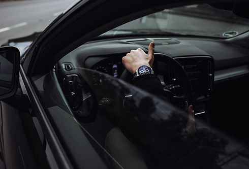 View through car window of a hand on a black steering wheel